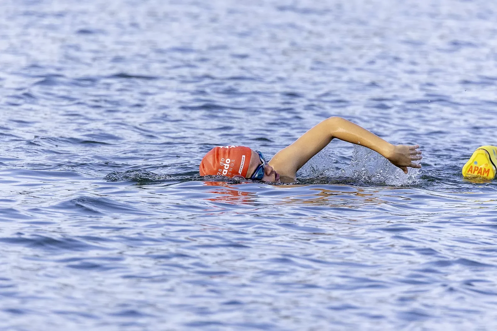 Nadador em nado livre em plano aberto, com boia de percurso ao fundo