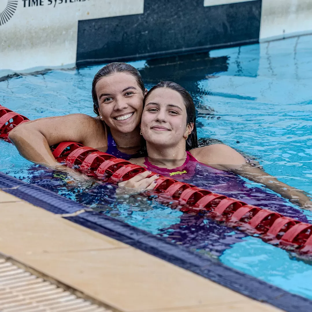 Duas nadadoras abraçadas na borda da piscina, sorrindo