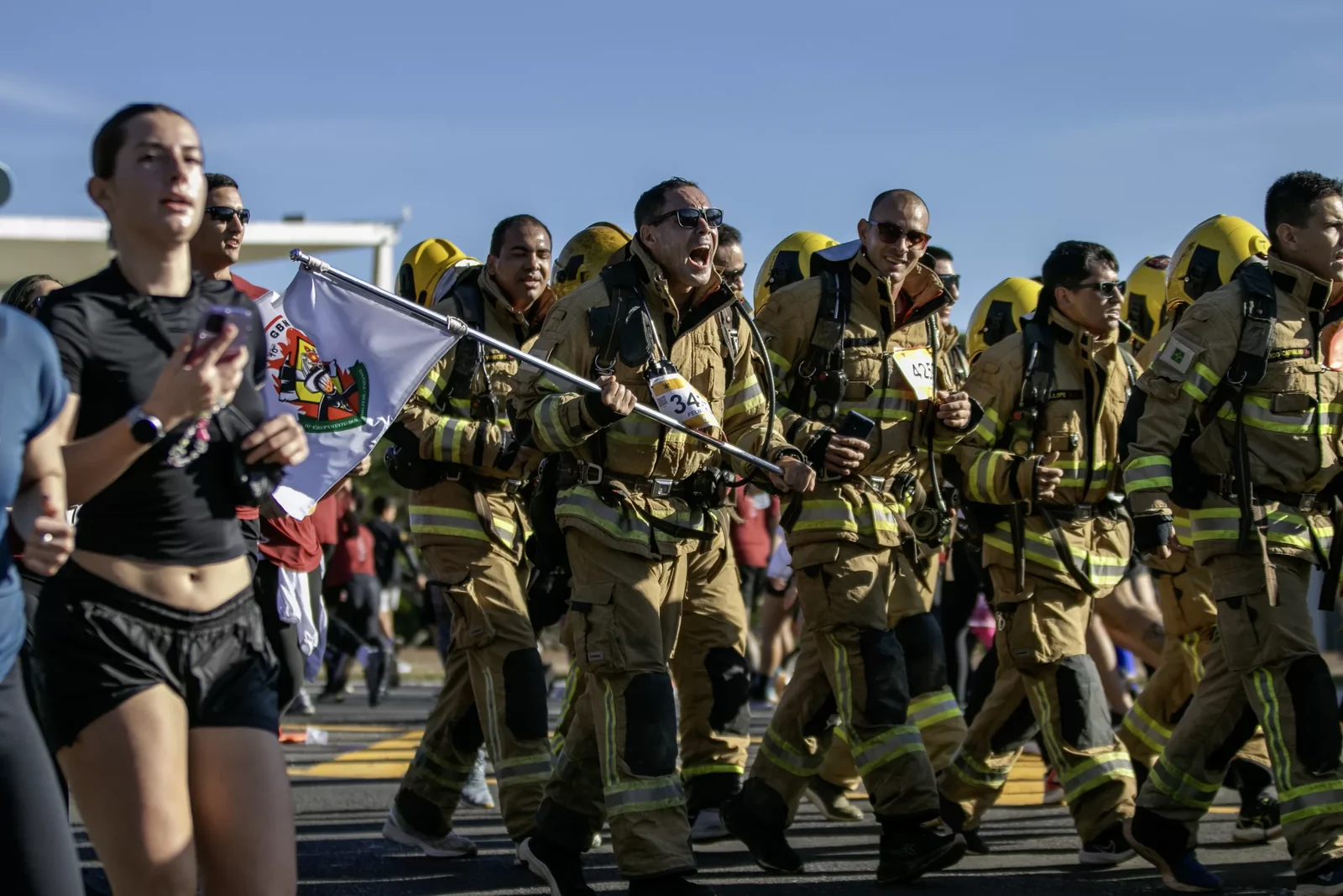 Bombeiros correndo fardados, com a bandeira do grupamento
