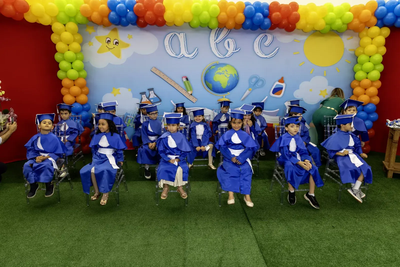 Turma de formandos sentada diante do painel da formatura, com balões