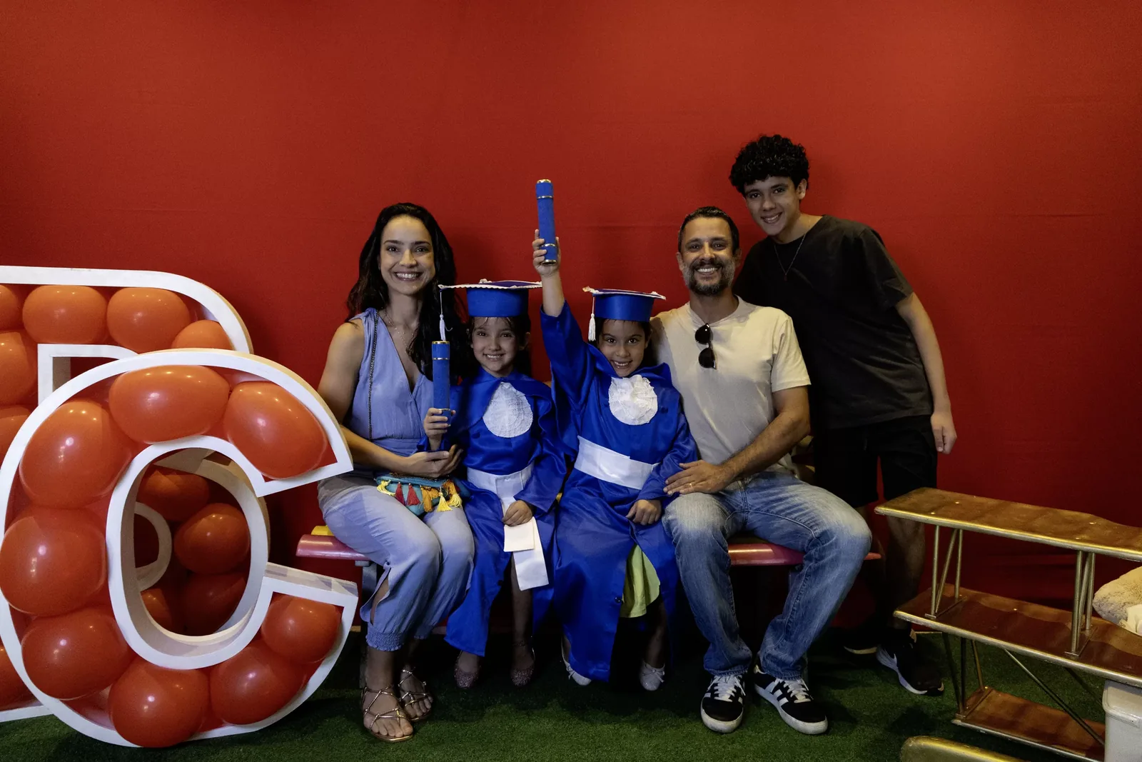 Família reunida com as formandas de beca no cenário da festa