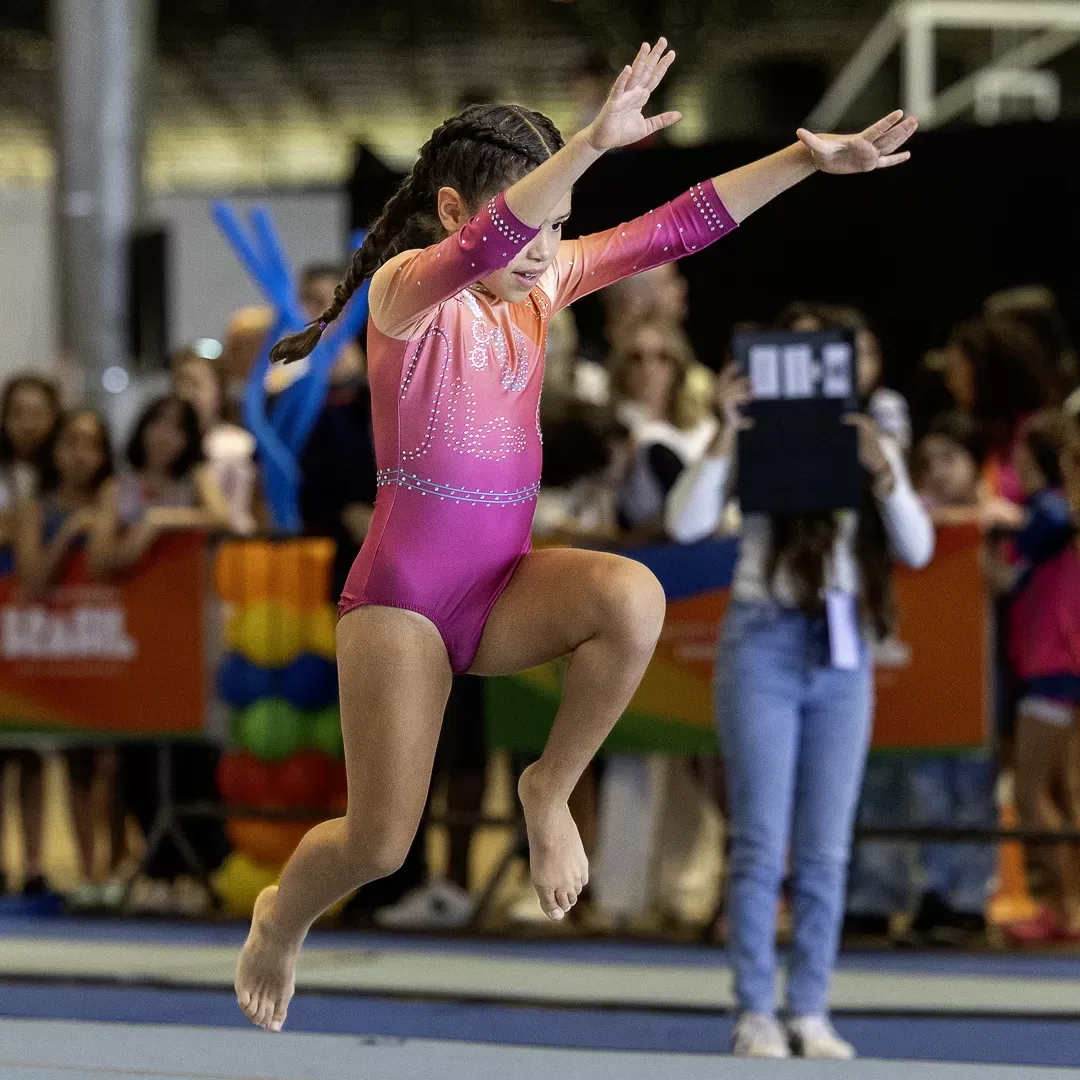 Ginasta finaliza o salto de solo com os braços abertos