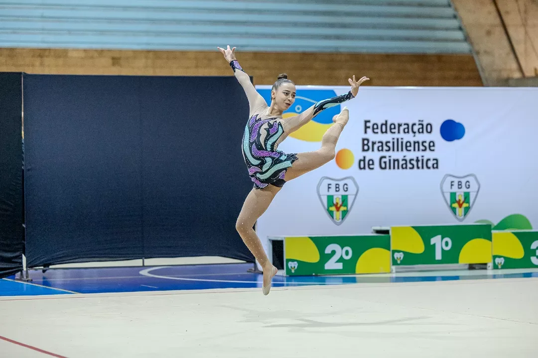 Ginasta em salto amplo diante do painel da FBG