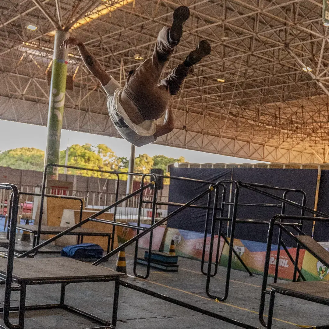 Atleta em salto mortal sob a estrutura do pavilhão