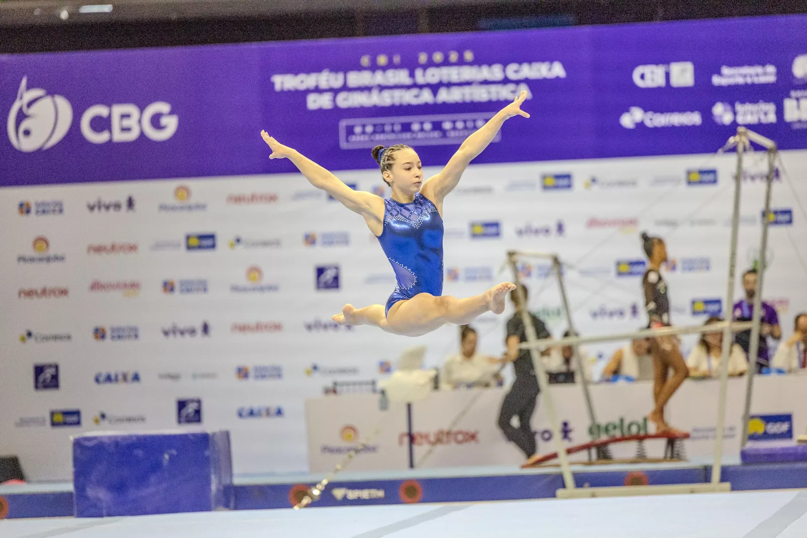 Ginasta em salto diante do painel do Troféu Brasil