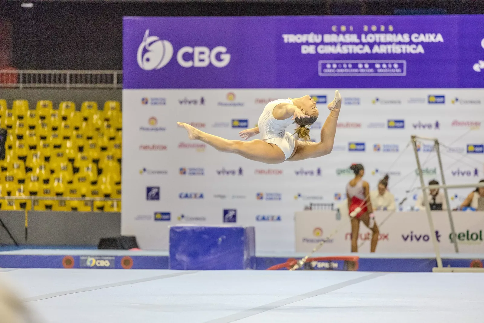 Ginasta em elemento de solo diante do painel do campeonato