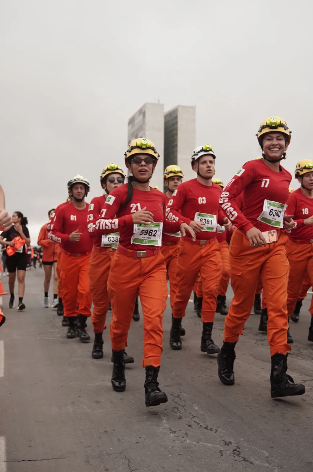 Bombeiros de uniforme laranja correndo em formação