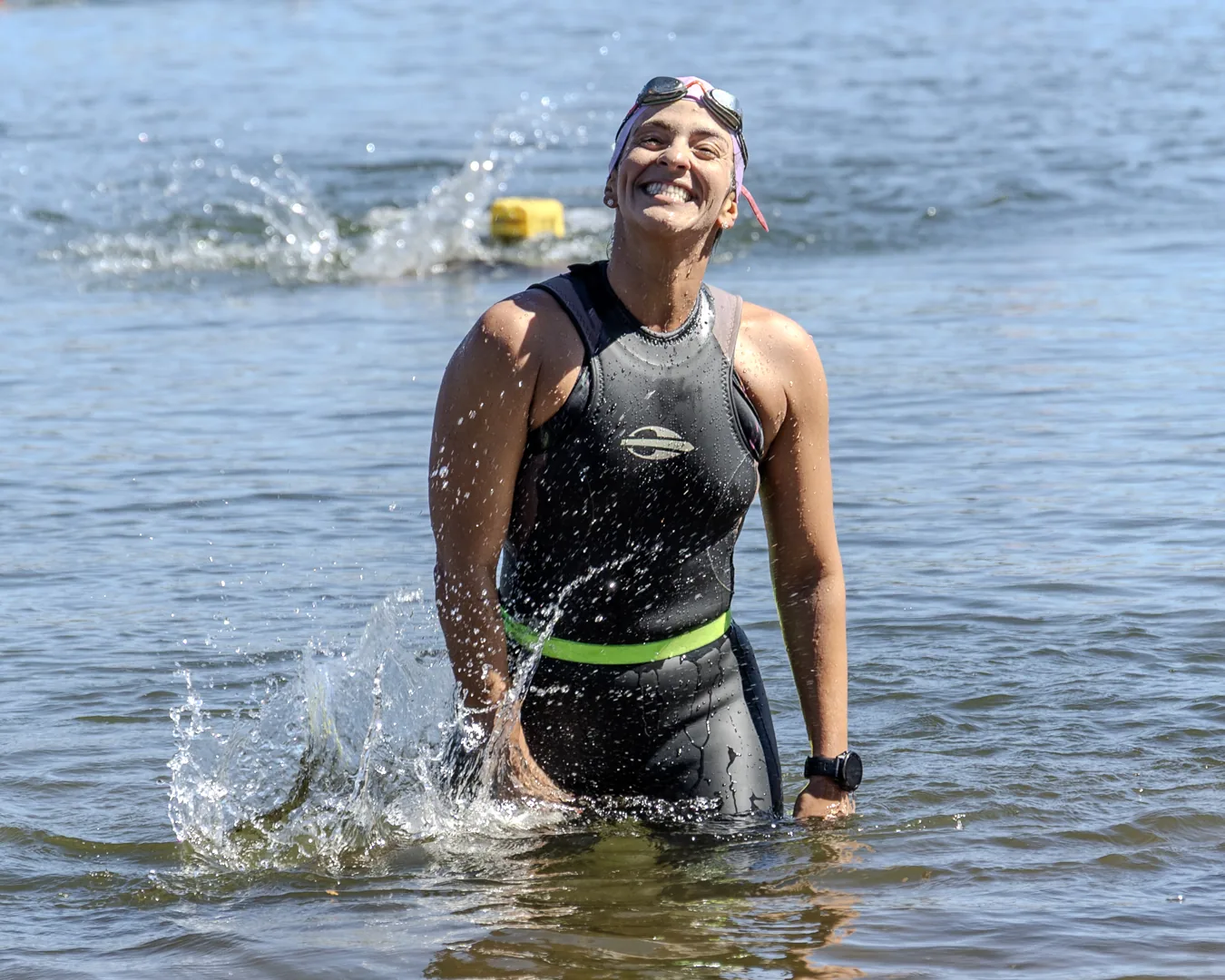 Nadadora de neoprene sorri ao sair do lago, levantando água