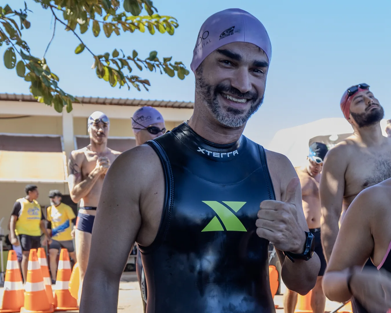 Nadador de neoprene sorri ao chegar, com outros nadadores atrás