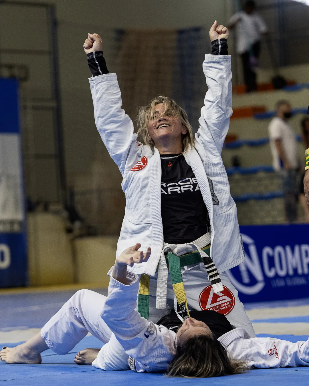 Atleta de kimono branco comemora ajoelhada com os braços erguidos