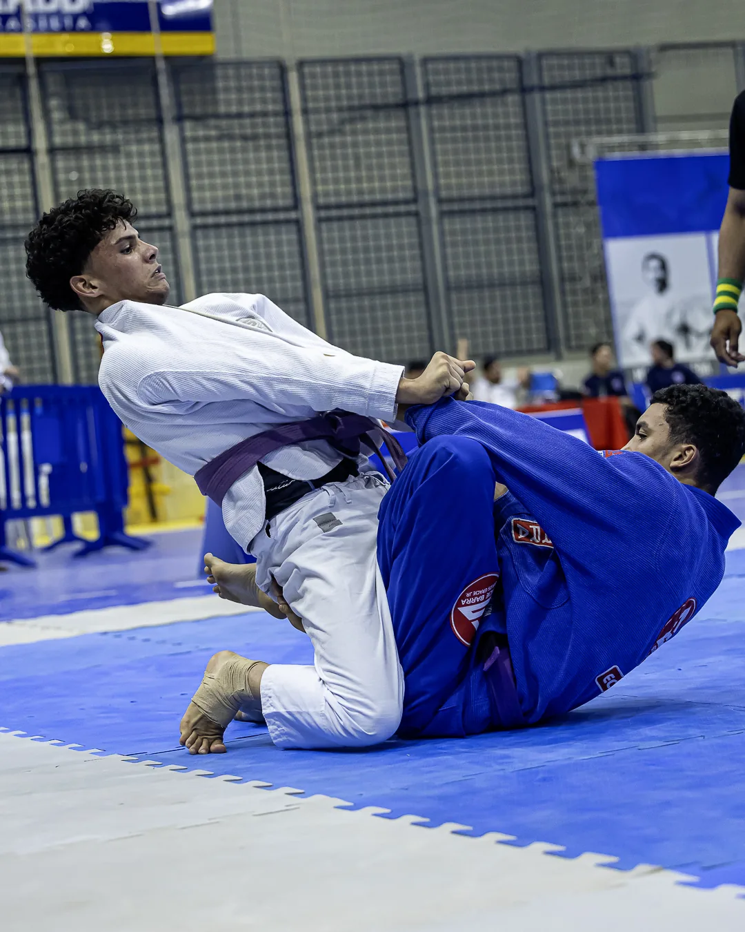 Dois atletas, de branco e de azul, disputam a pegada em pé