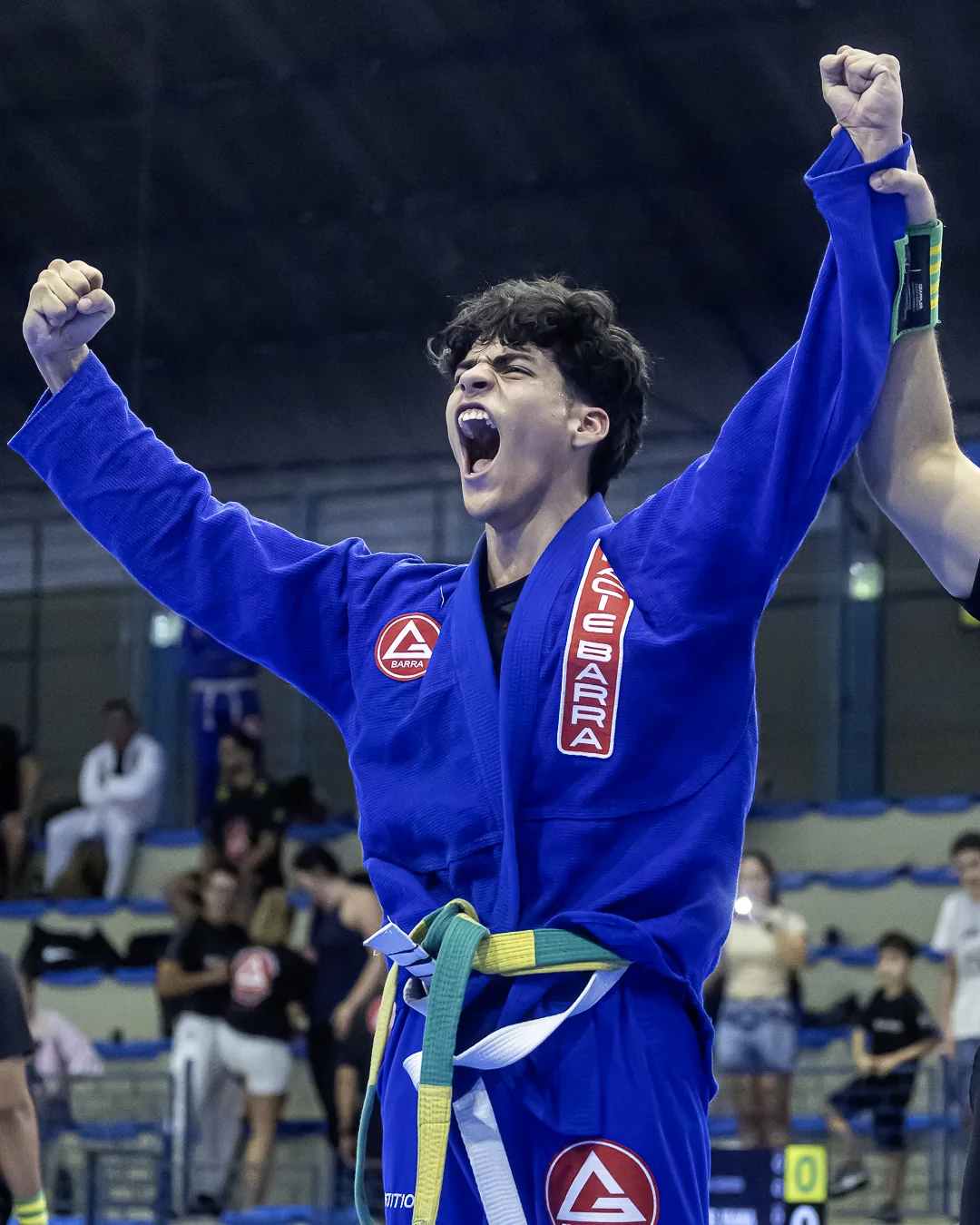 Jovem de kimono azul grita com os braços erguidos após a vitória