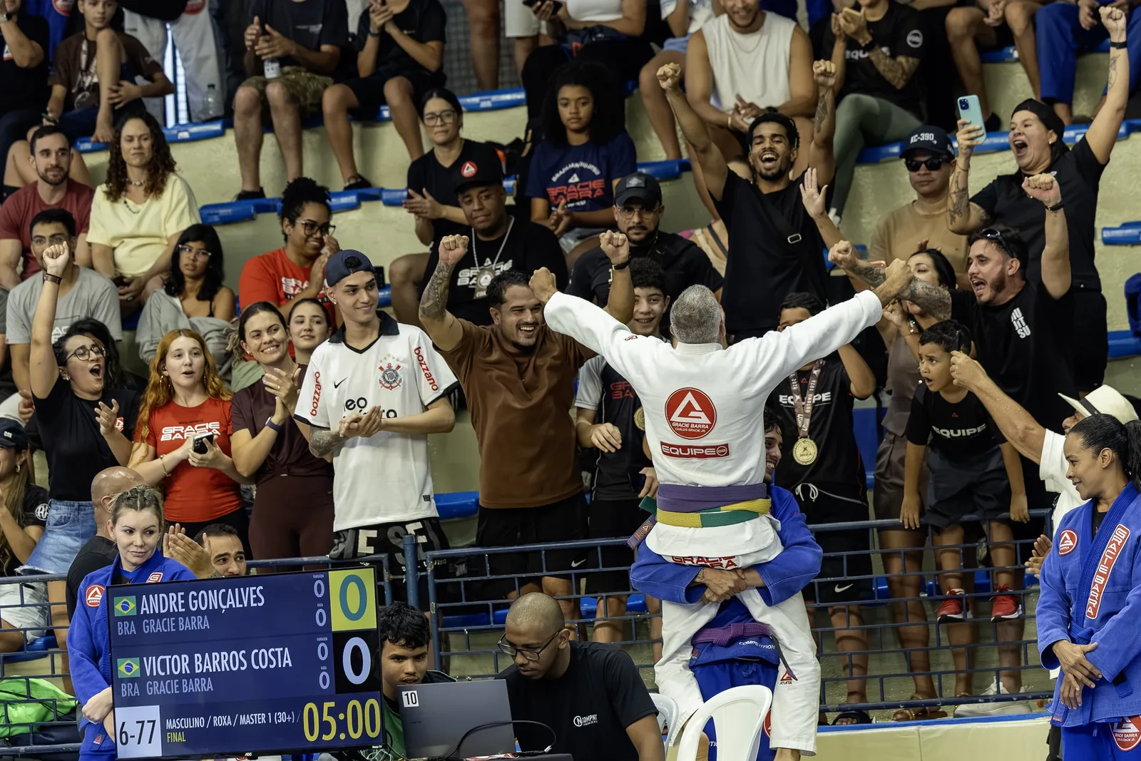 Torcida de pé na arquibancada comemora enquanto o atleta de branco ergue os braços