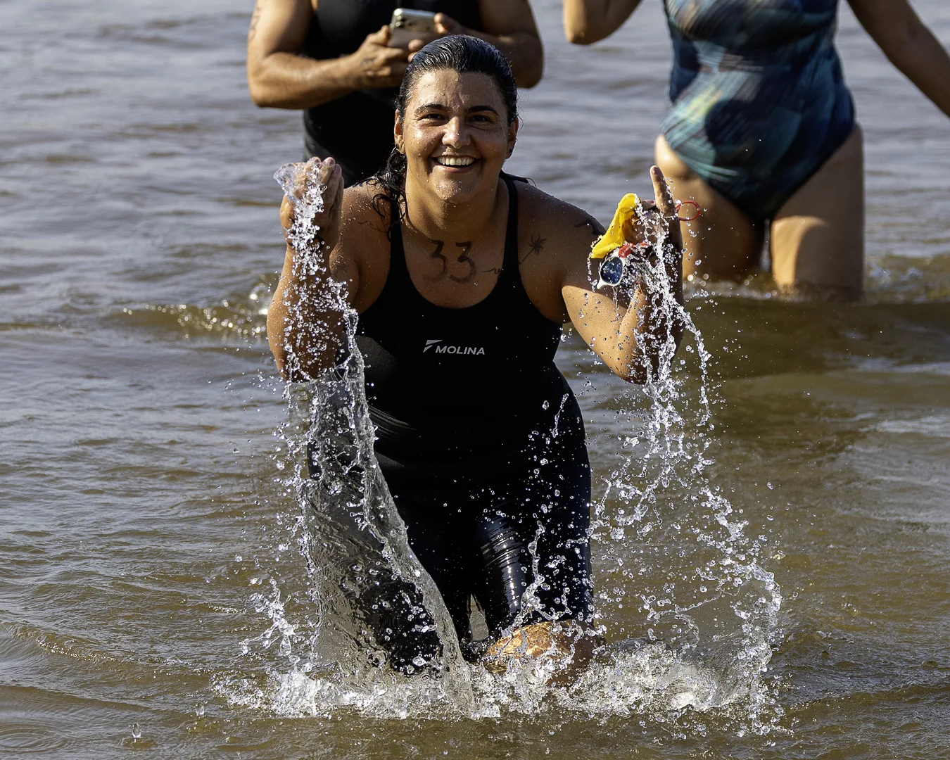 Nadadora sorrindo ao sair do lago, com água escorrendo dos braços