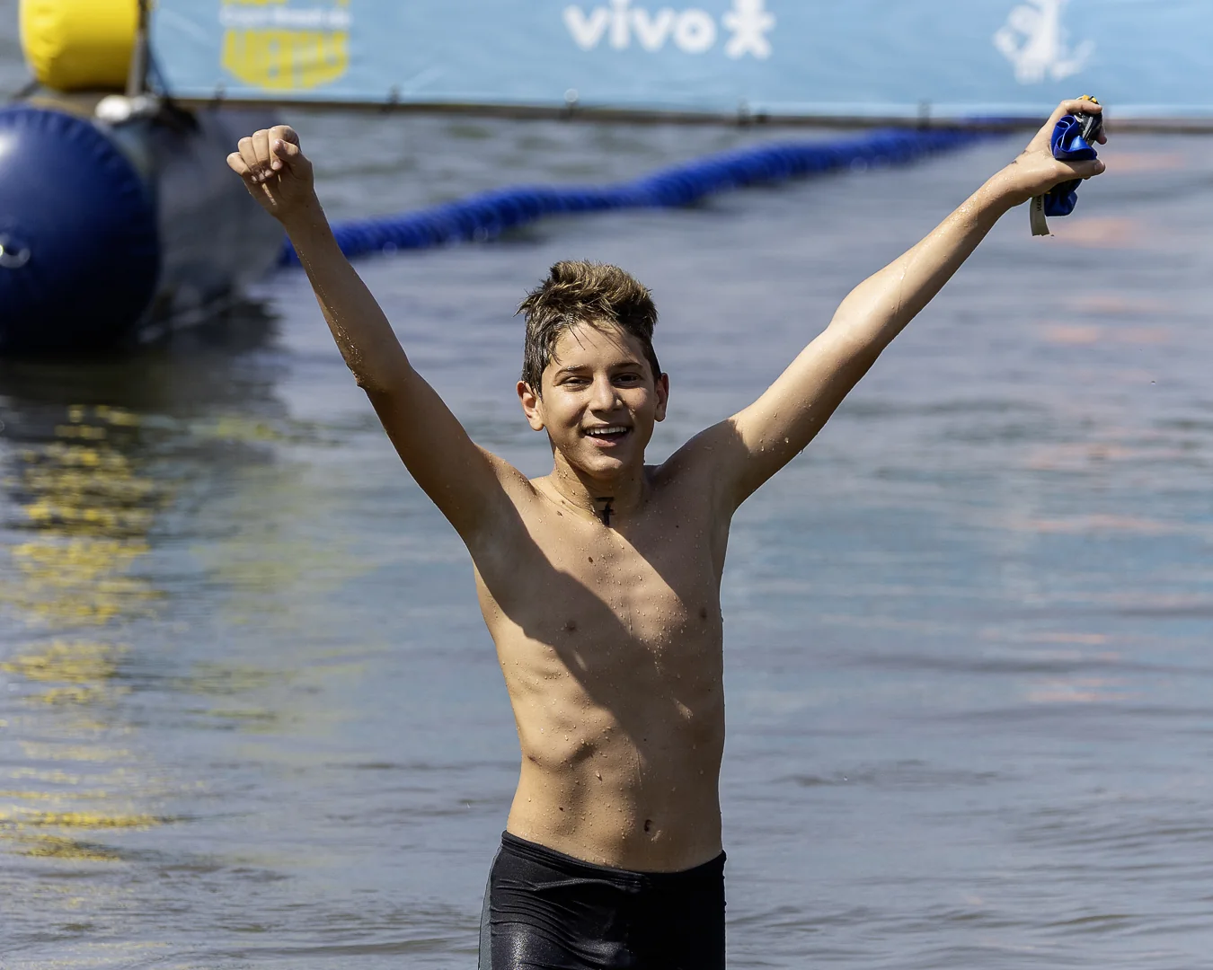 Menino comemora de braços erguidos dentro do lago após completar a prova