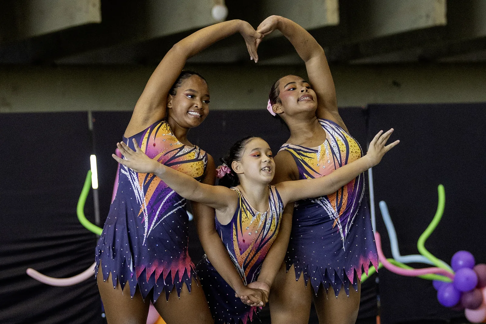 Trio de ginastas em pose com os braços formando um coração