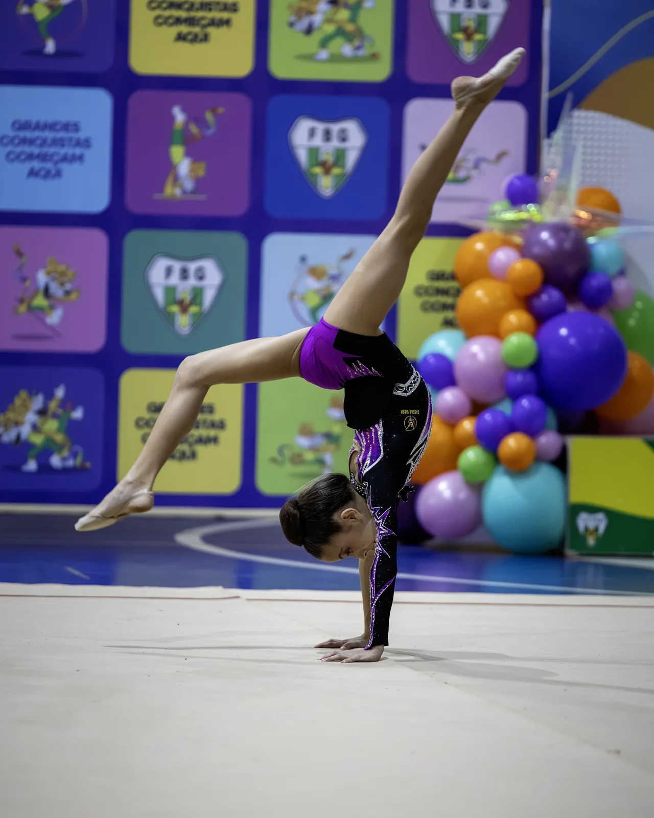 Ginasta invertida em apoio sobre uma das mãos, com as pernas abertas no alto