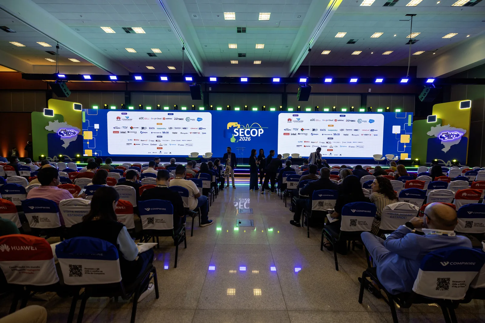 Plenária lotada do SECOP 2026 vista do fundo do auditório, com o palco iluminado ao longe