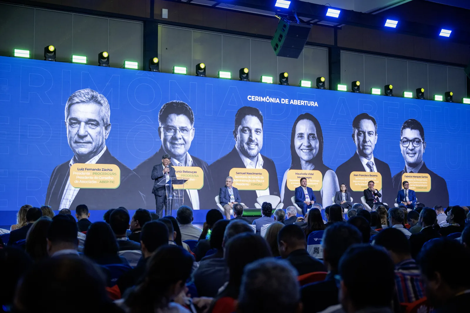 Cerimônia de abertura com os participantes da mesa no telão, diante do auditório
