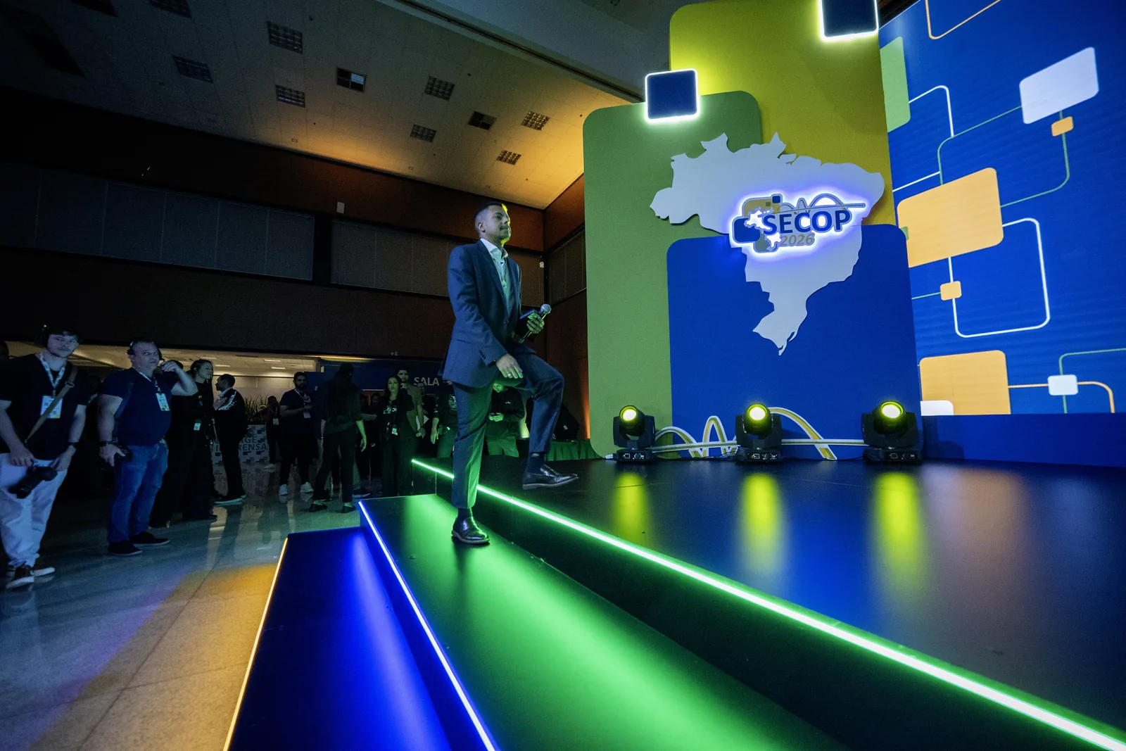 Apresentador caminha pela passarela do palco, com o público ao fundo