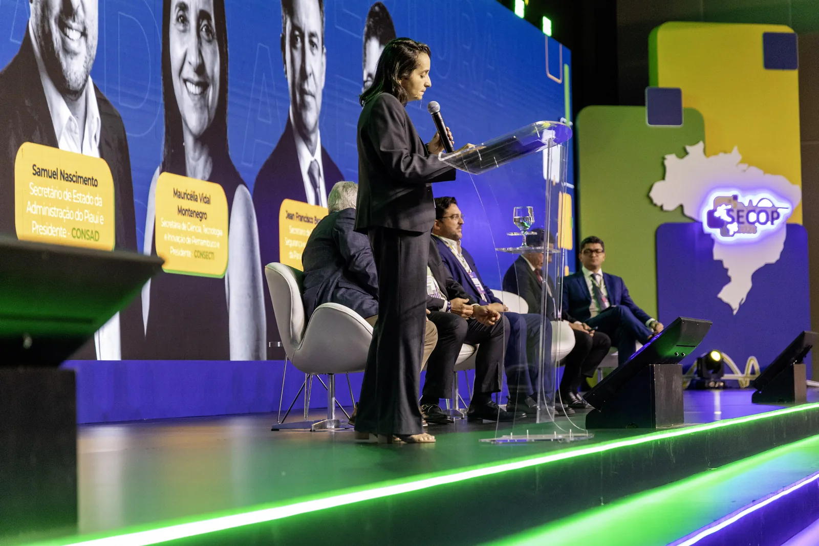 Mediadora conduz painel com convidados sentados no palco