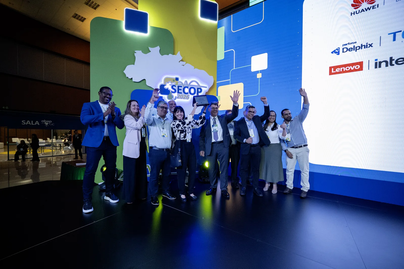 Equipe premiada comemora de braços erguidos no palco