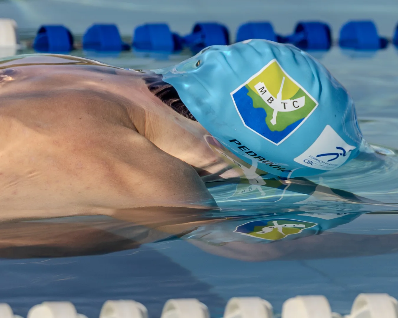 Nadador deslizando com o reflexo da touca na superfície ainda lisa da piscina