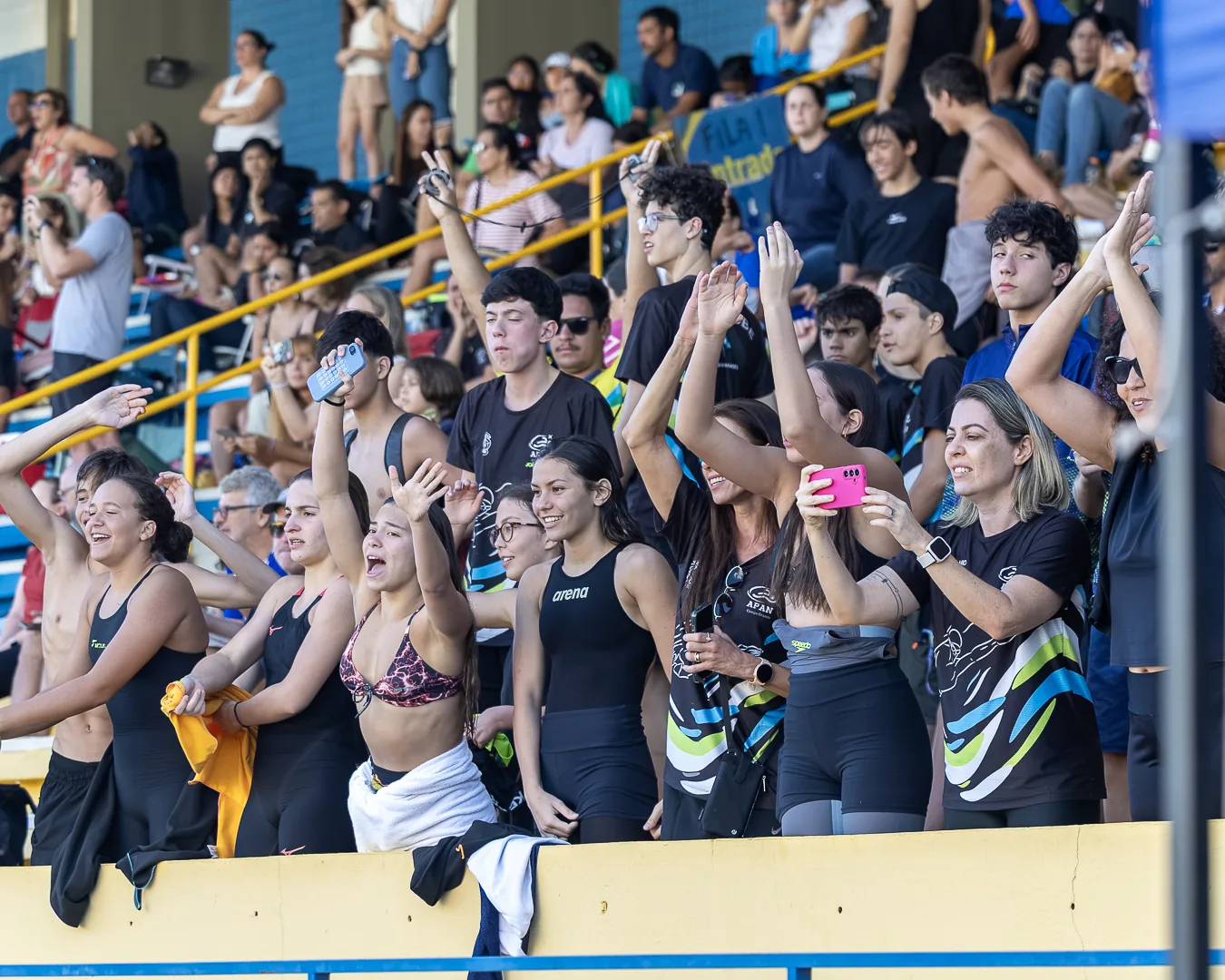 Torcida de um clube na arquibancada, de pé, gritando e filmando com o celular