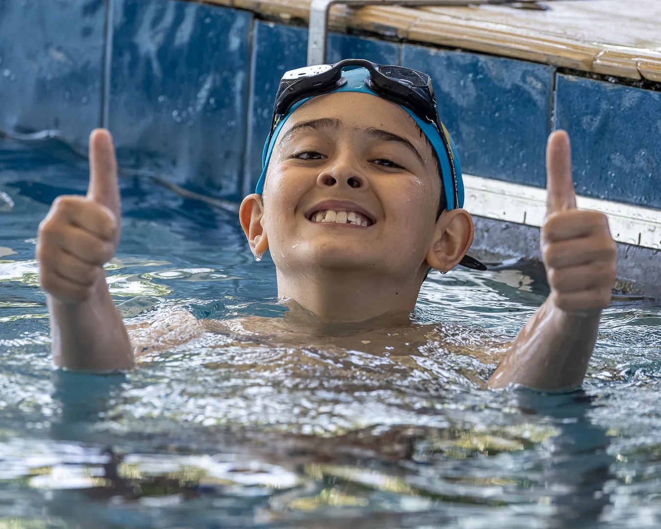 Nadador sorri e faz joinha com as duas mãos dentro da piscina