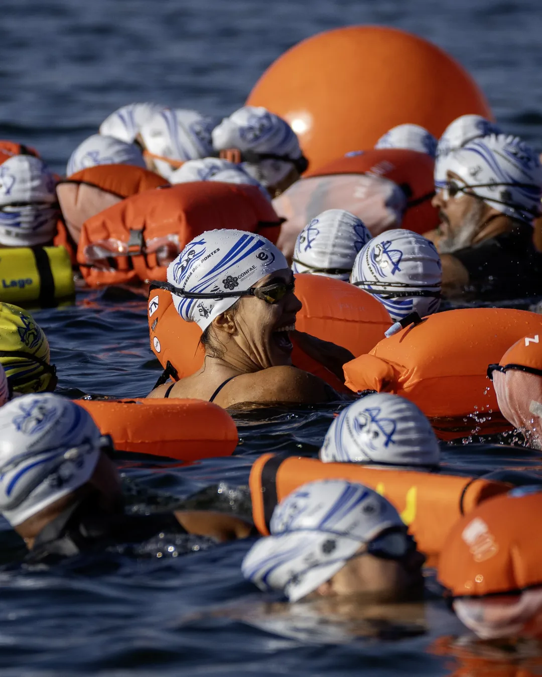 Grupo de nadadores de touca branca e boias laranja aguardando dentro do Lago Paranoá antes da largada