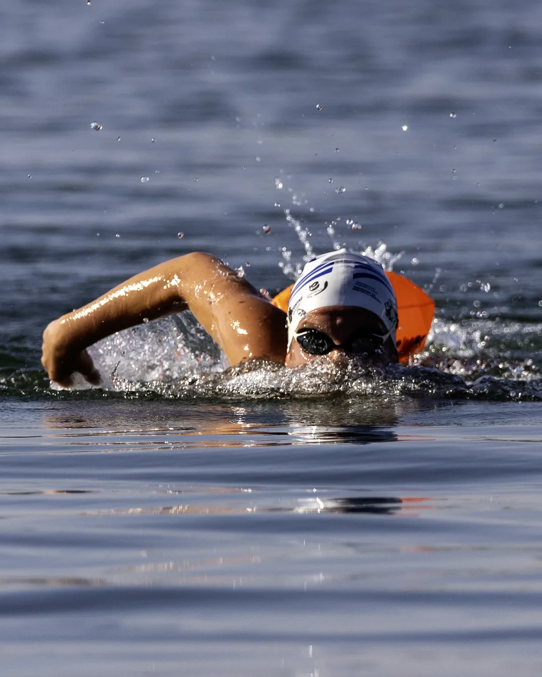 Nadador em nado crawl no lago ao sol da manhã, com boia laranja presa à cintura
