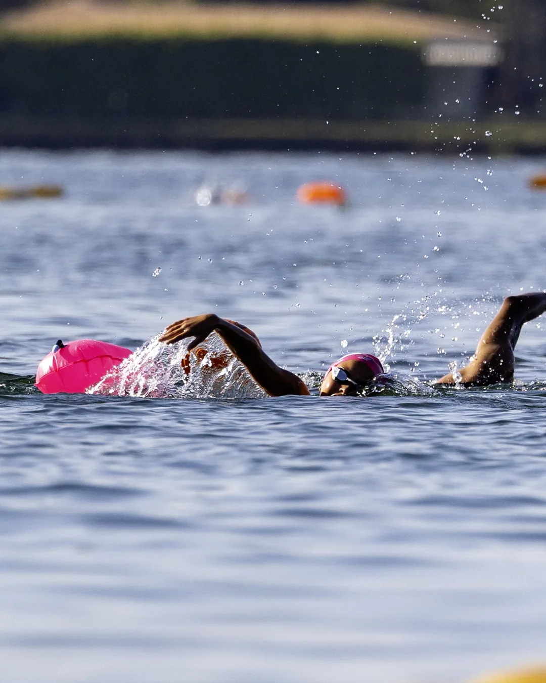 Dois nadadores lado a lado no percurso, com a orla do Lago Paranoá ao fundo