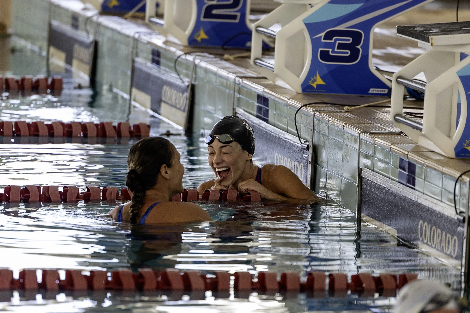 Duas nadadoras master conversando e rindo na borda da piscina