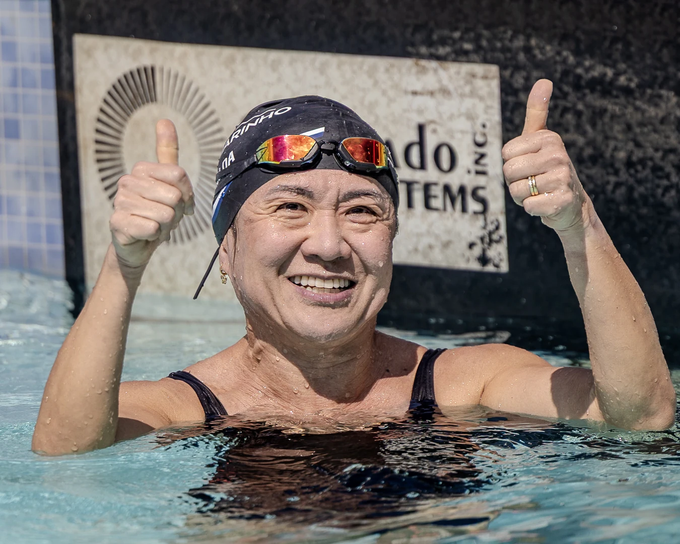 Nadadora master sorrindo dentro da piscina com os dois polegares erguidos