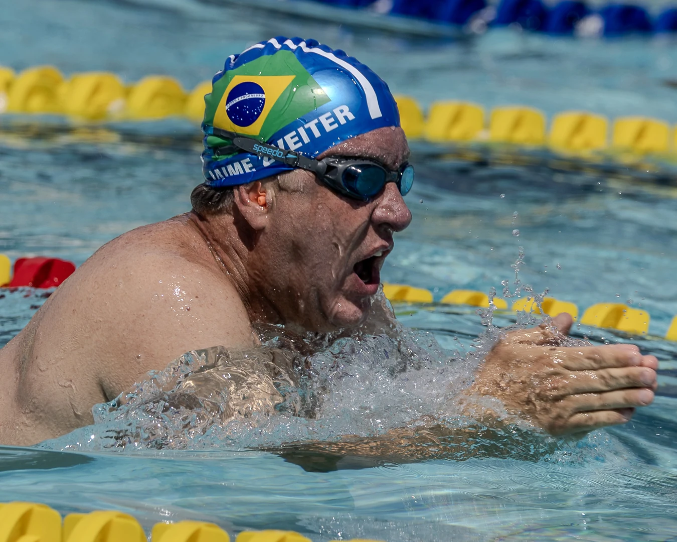 Nadador master com touca do Brasil emergindo na braçada de peito